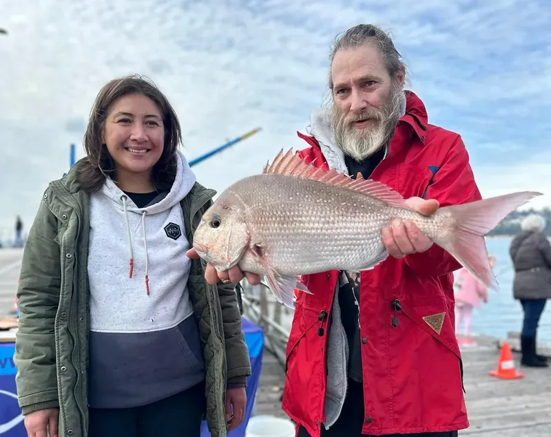 A support worker and participant on a pier, proudly showing off a large snapper caught on a fishing day